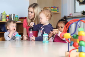 erzieherin-am-tisch-kinder-trinken-aus-trinkflasche-mit-spielzeug