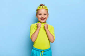 joyous-small-female-child-raises-clenched-fists-rejoices-successful-swimming-wears-goggles-bright-clothes-has-toothy-smile-enjoys-her-favourite-hobby-during-summer-holiday-happy-childhood